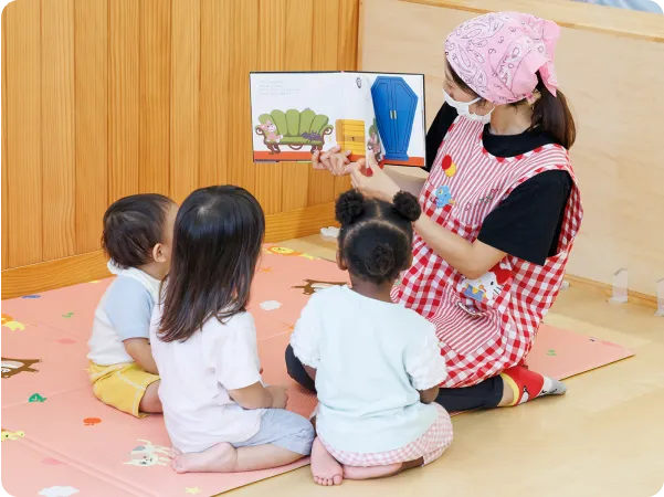 年齢の違う子供たちが一緒に絵本を読んでもらっている画像