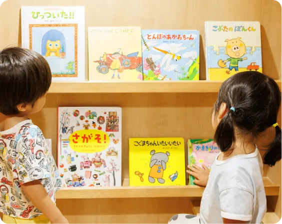 園児が棚に並んでいる絵本を見ている画像